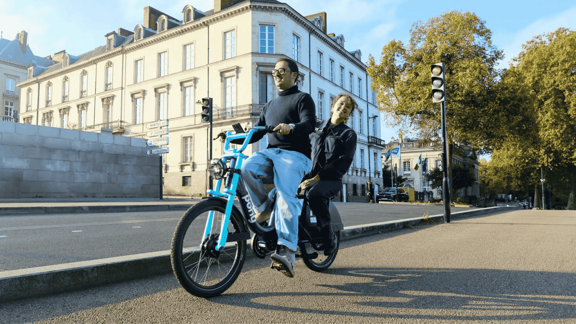 Deux usagers circulent sur un vélo électrique Double Pony de Pony sur une avenue nantaise bordée d’immeubles historiques
