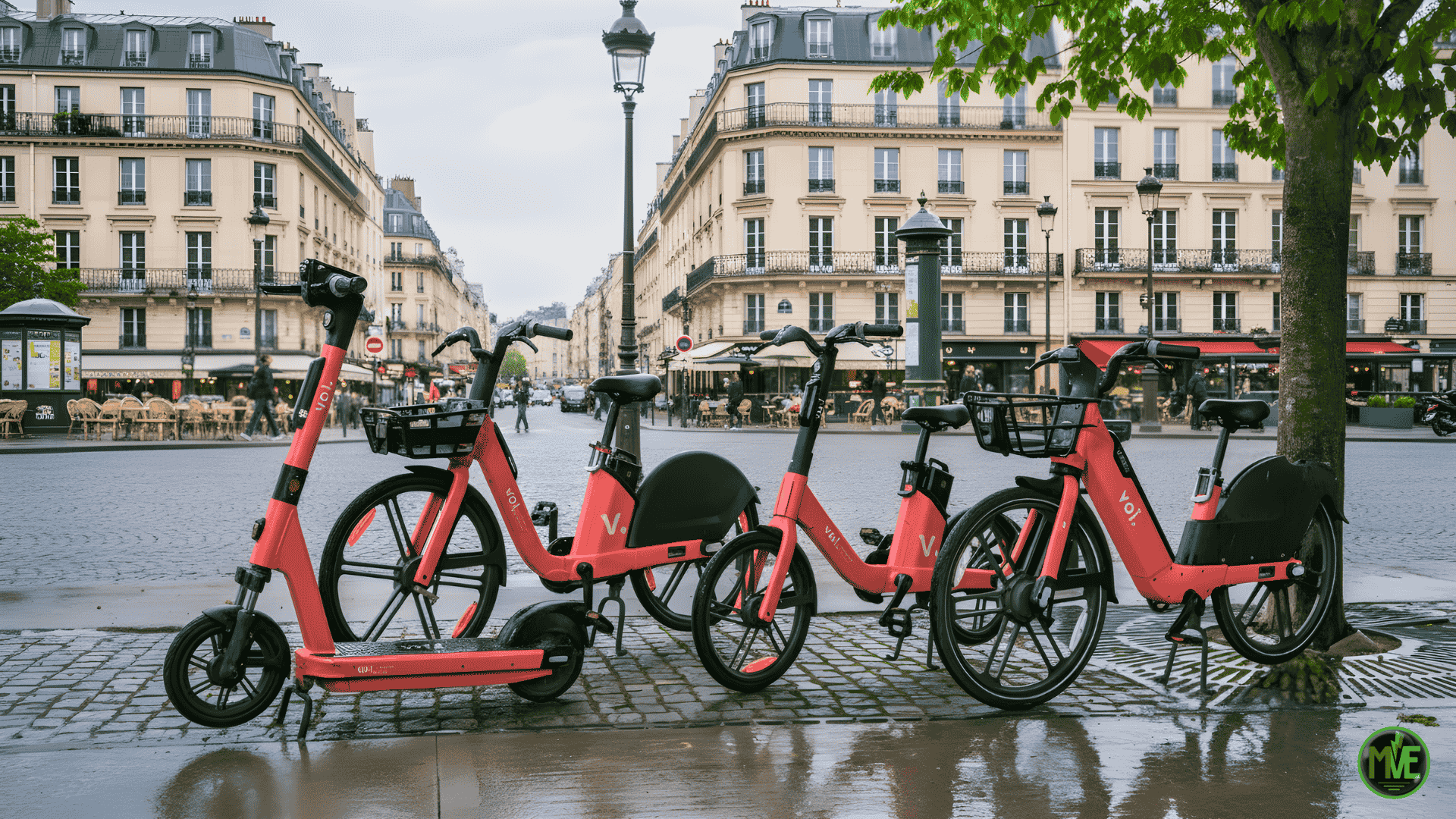 Vélos électriques Voi rouges (et une trottinette) alignés sur pavés mouillés à Paris, devant immeubles haussmanniens — service de location de VAE