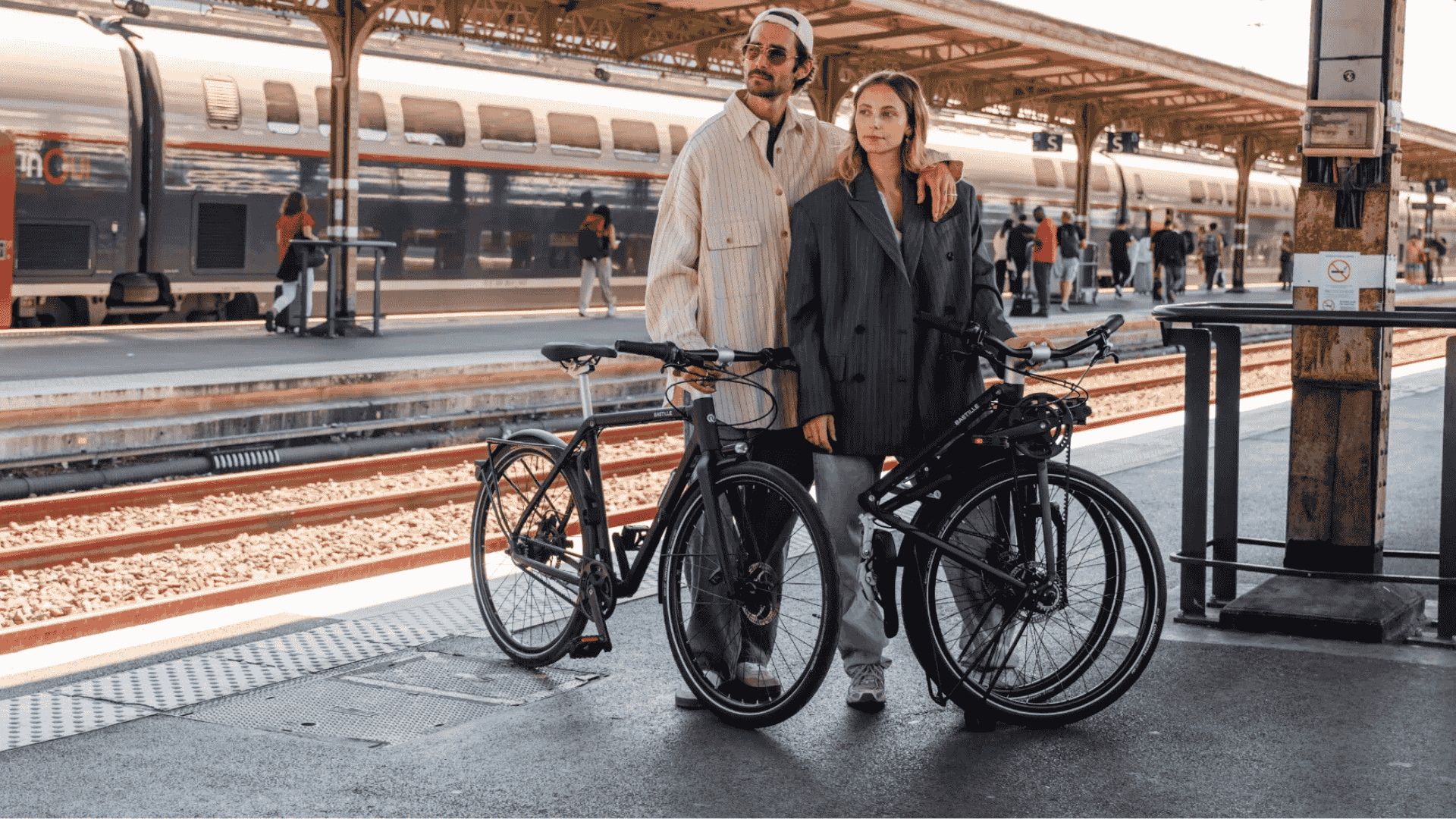 Deux utilisateurs avec leur vélo électrique pliant Bastille E sur un quai de gare, prêt à embarquer en train