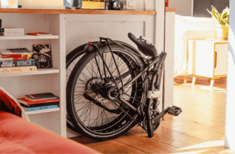 Vélo électrique pliant Bastille E rangé sous un bureau, illustrant son format compact et son pliage rapide.