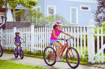 Trois enfants roulant sur des vélos Trek devant une maison, portant des casques, dans un quartier résidentiel