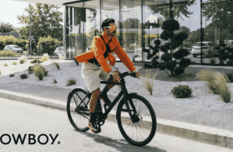 Cycliste roulant sur un vélo électrique Cowboy devant un bâtiment vitré, en milieu urbain.